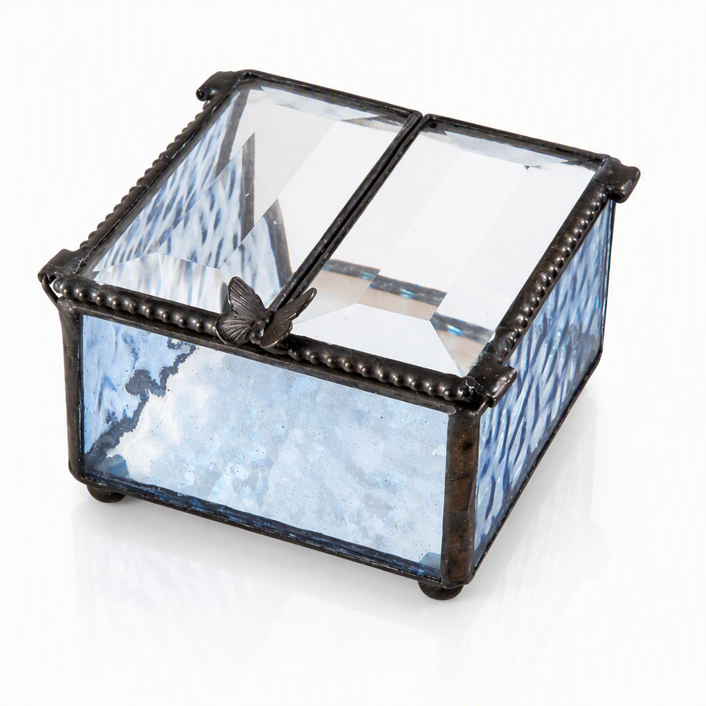 A square glass jewelry box with a hinged lid, featuring light blue textured glass sides, clear glass panels on top, and a dark metal frame with a butterfly ornament on the lid.